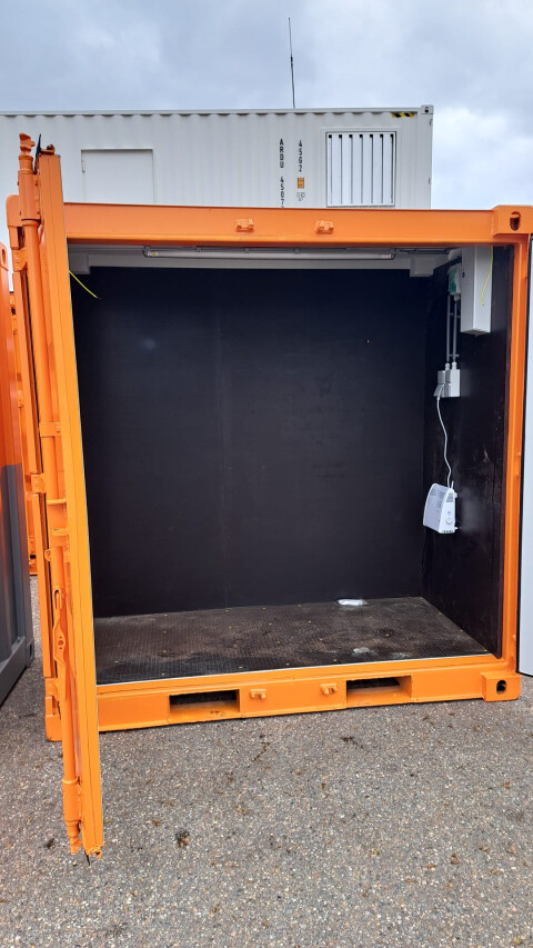 Oranje zeecontainer met open zijde en zwarte binnenwand, voorzien van verlichting en elektra-installatie