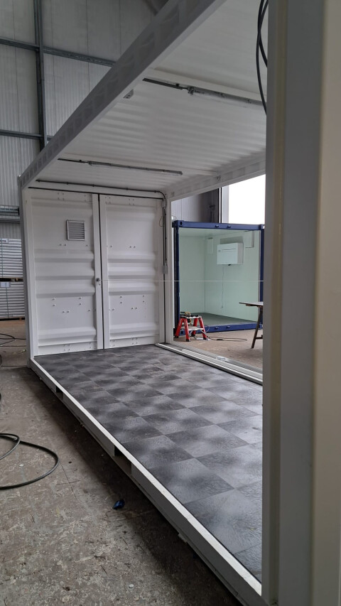 Witte zeecontainer in aanbouw met open zijwand en afgewerkte vloer in werkplaats van Van Doorn Container Modifications